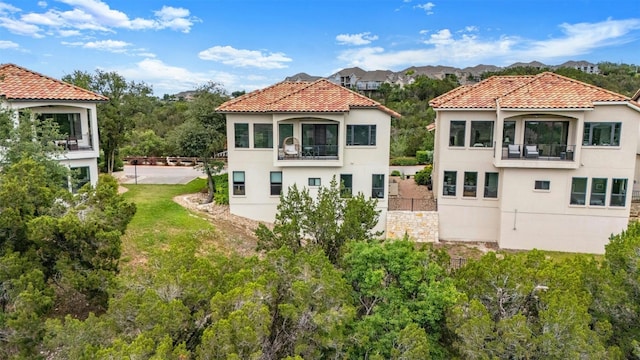 back of property with stucco siding, a tiled roof, a balcony, and fence