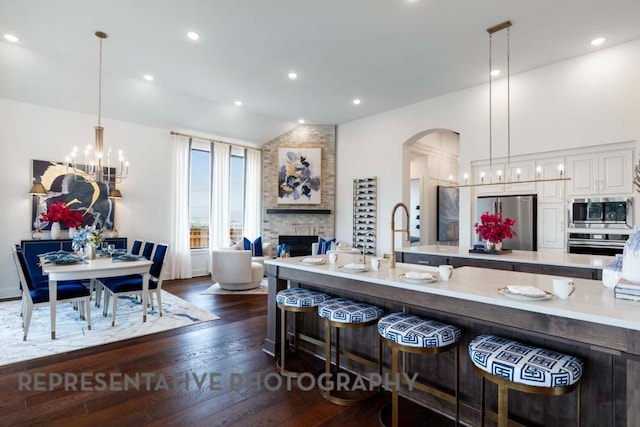 kitchen with a breakfast bar, arched walkways, appliances with stainless steel finishes, light countertops, and dark wood-style flooring