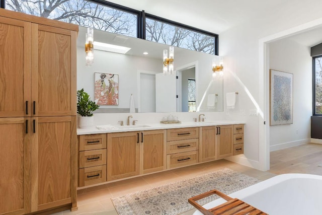 bathroom with an inviting chandelier, a skylight, double vanity, a sink, and tile patterned floors