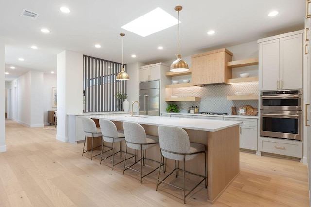 kitchen featuring visible vents, a center island with sink, light countertops, appliances with stainless steel finishes, and open shelves