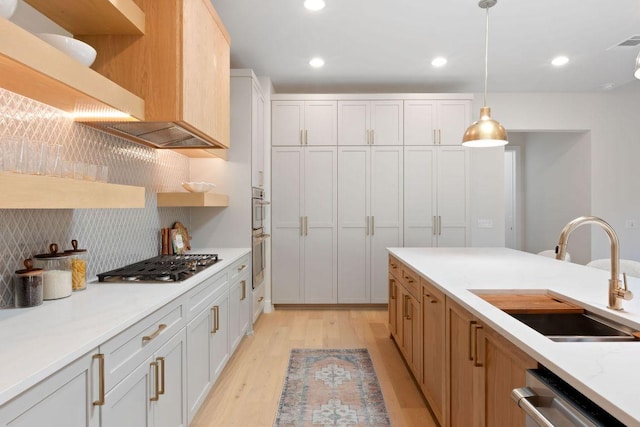 kitchen featuring light wood finished floors, open shelves, stainless steel appliances, hanging light fixtures, and a sink