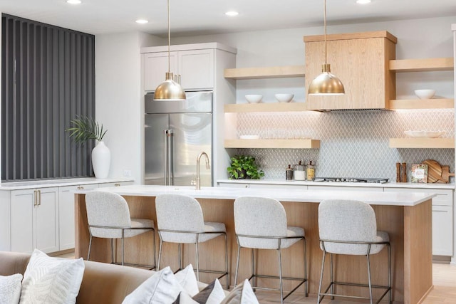 kitchen featuring an island with sink, light countertops, decorative backsplash, built in fridge, and open shelves