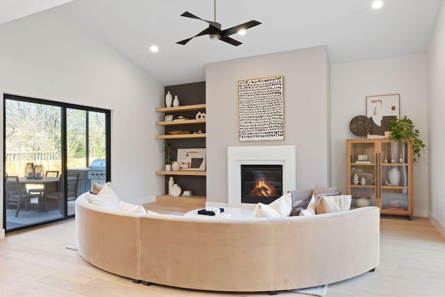 living area with a glass covered fireplace, lofted ceiling, light wood-style floors, and ceiling fan