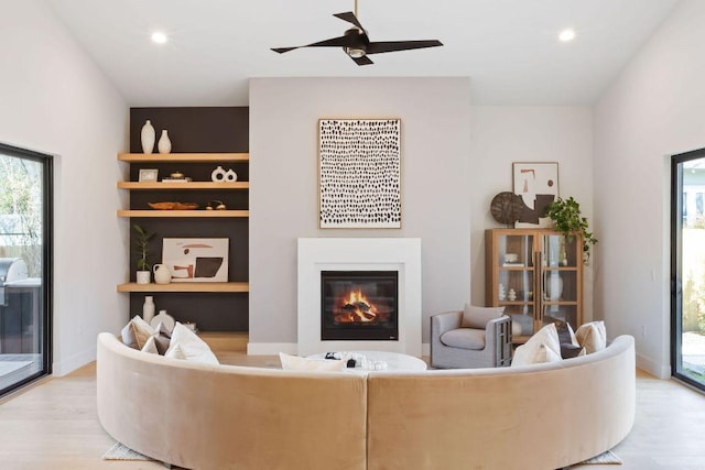 living room featuring baseboards, recessed lighting, light wood-style flooring, a glass covered fireplace, and a ceiling fan