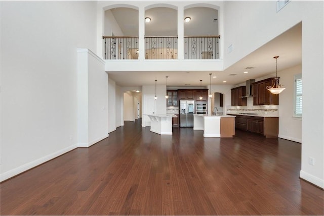 unfurnished living room featuring dark wood-style floors, baseboards, a towering ceiling, and a sink