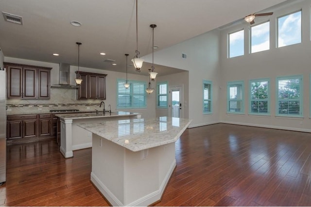 kitchen with a spacious island, visible vents, wall chimney range hood, decorative backsplash, and dark wood-style flooring