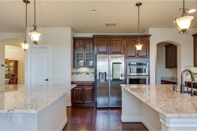 kitchen with a large island, a sink, stainless steel appliances, arched walkways, and dark wood-style flooring