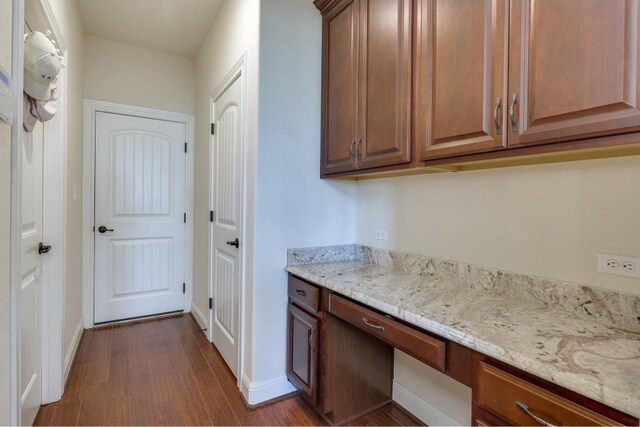 kitchen featuring dark wood-style floors, built in desk, baseboards, and light stone countertops