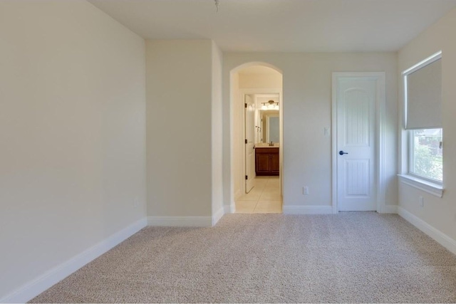 empty room with baseboards, arched walkways, and light colored carpet