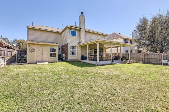 back of property with a fenced backyard, a lawn, a chimney, and a patio