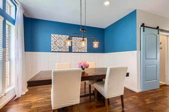 dining room with a barn door, wood finished floors, and a wainscoted wall