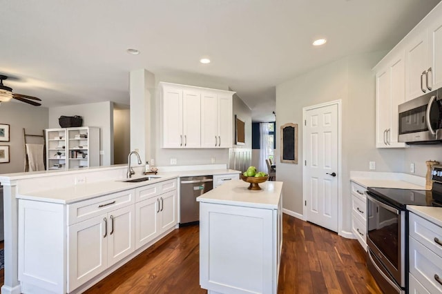 kitchen with dark wood finished floors, a peninsula, a sink, stainless steel appliances, and light countertops