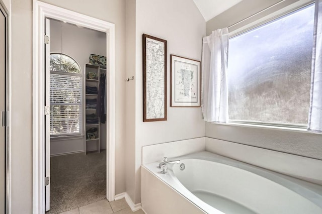 bathroom with a spacious closet, tile patterned floors, baseboards, vaulted ceiling, and a bath