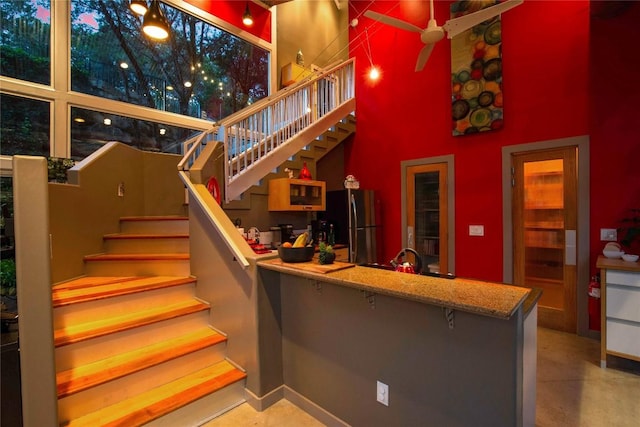 stairs with ceiling fan, a towering ceiling, and baseboards