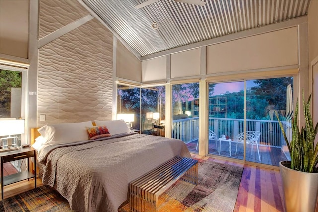 bedroom featuring access to exterior, multiple windows, high vaulted ceiling, and wood finished floors