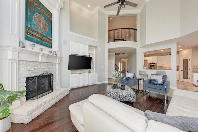 living room with hardwood / wood-style floors, baseboards, a fireplace with raised hearth, ceiling fan, and crown molding