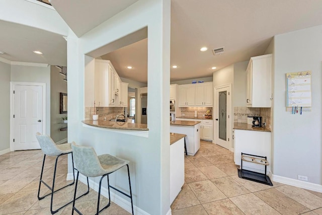 kitchen with a breakfast bar, backsplash, a peninsula, white cabinets, and baseboards