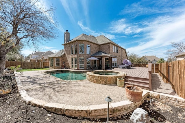 back of house featuring a patio, a fenced backyard, a chimney, a deck, and brick siding