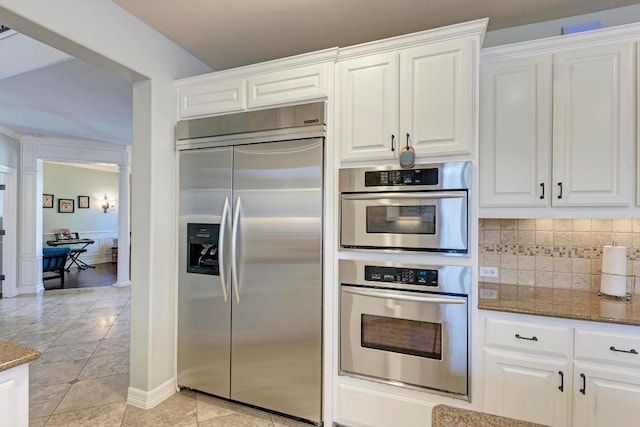 kitchen with dark stone counters, white cabinets, backsplash, and stainless steel appliances