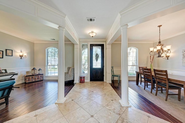 foyer featuring light tile patterned floors, visible vents, wainscoting, and ornate columns