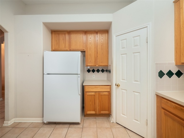 kitchen featuring light tile patterned floors, decorative backsplash, light countertops, and freestanding refrigerator