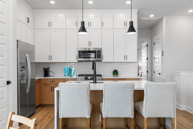 kitchen with an island with sink, light wood-style flooring, stainless steel appliances, light countertops, and backsplash