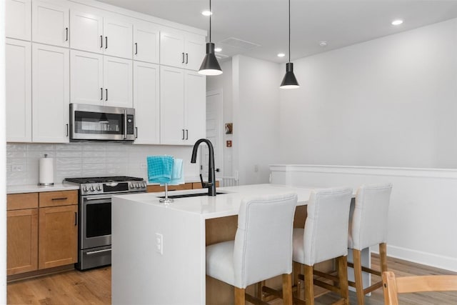 kitchen with an island with sink, a sink, tasteful backsplash, appliances with stainless steel finishes, and light wood finished floors