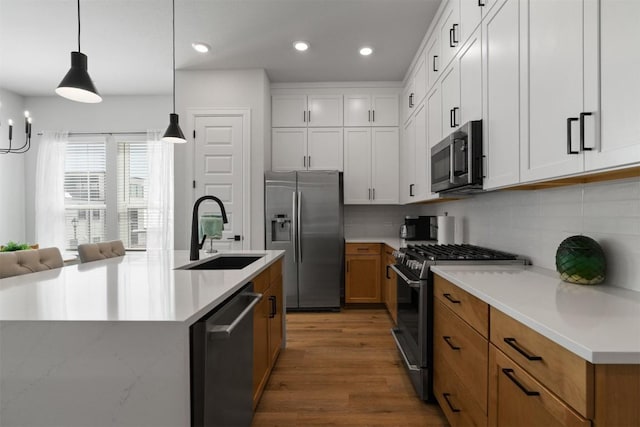 kitchen featuring tasteful backsplash, pendant lighting, appliances with stainless steel finishes, wood finished floors, and a sink