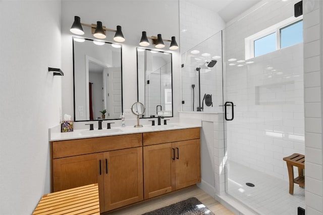 bathroom with a stall shower, double vanity, a sink, and wood finished floors
