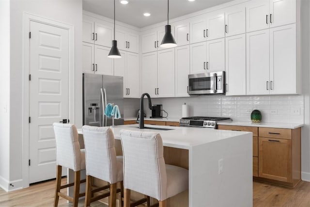 kitchen with tasteful backsplash, a center island with sink, light wood-style flooring, appliances with stainless steel finishes, and a sink