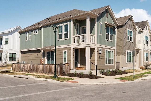 exterior space featuring fence, a shingled roof, board and batten siding, and a balcony