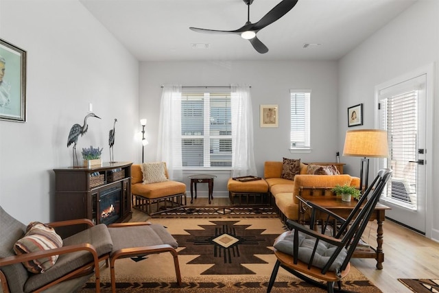 living area featuring visible vents, light wood-type flooring, ceiling fan, and a glass covered fireplace