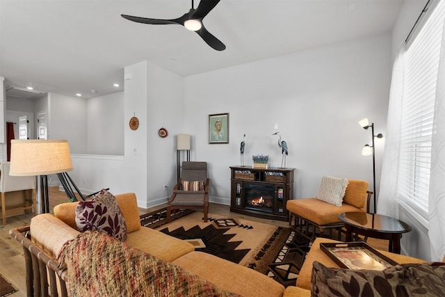 living room with a glass covered fireplace, wood finished floors, recessed lighting, baseboards, and ceiling fan