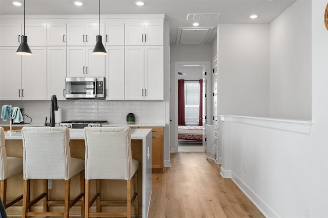 kitchen featuring stainless steel microwave, tasteful backsplash, light wood-style flooring, light countertops, and recessed lighting