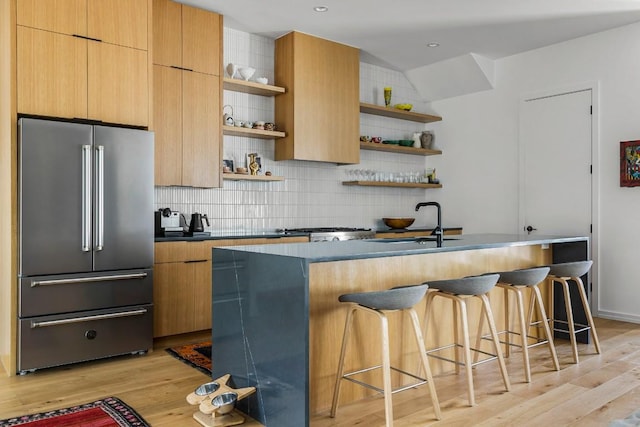 kitchen featuring tasteful backsplash, light wood finished floors, open shelves, high end fridge, and a sink