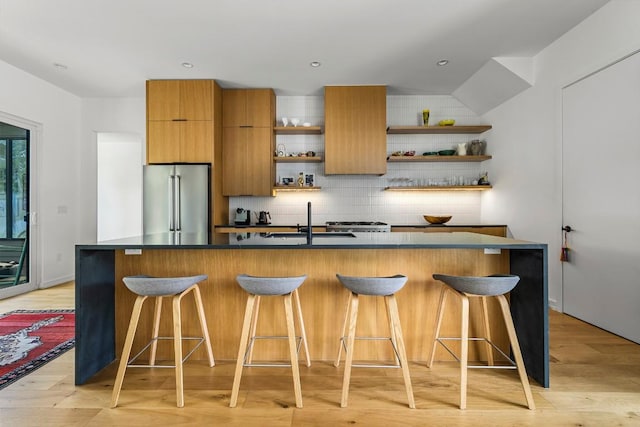 kitchen featuring light wood finished floors, open shelves, decorative backsplash, high end fridge, and a sink