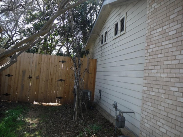 view of property exterior with brick siding, central AC unit, and fence