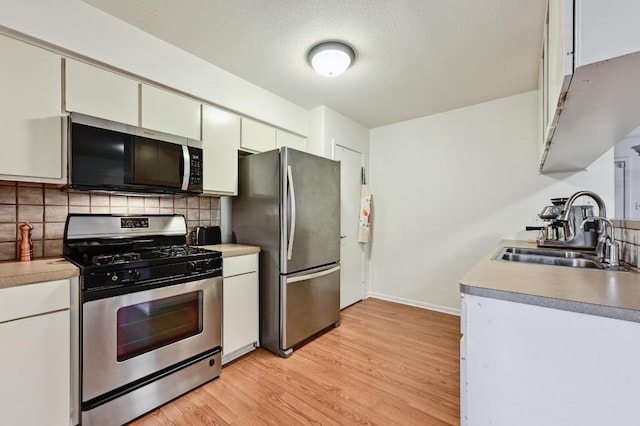 kitchen with light wood-style flooring, a sink, tasteful backsplash, a textured ceiling, and appliances with stainless steel finishes