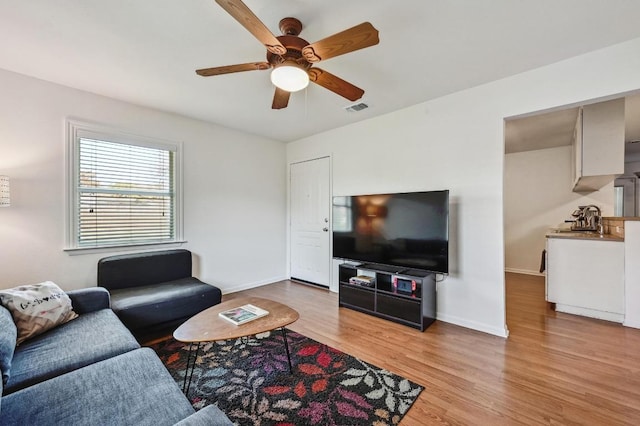 living area with light wood-style flooring, a ceiling fan, visible vents, and baseboards