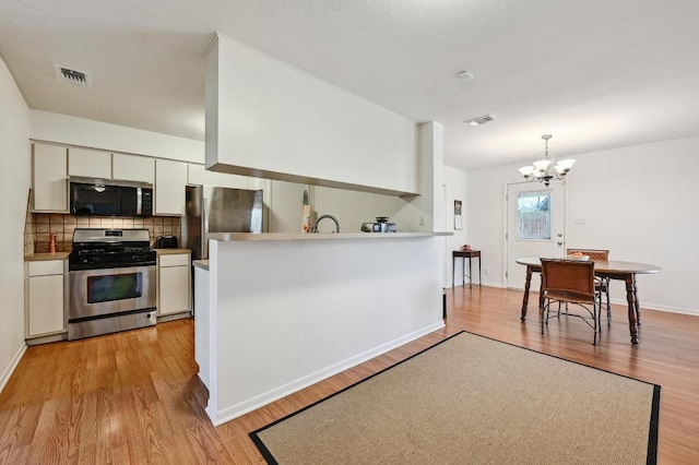 kitchen with tasteful backsplash, light wood-style flooring, stainless steel appliances, a notable chandelier, and white cabinetry