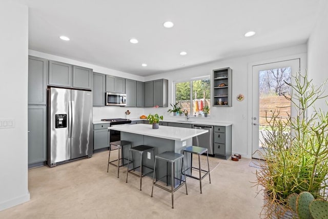 kitchen with gray cabinetry, a sink, a kitchen breakfast bar, appliances with stainless steel finishes, and light countertops