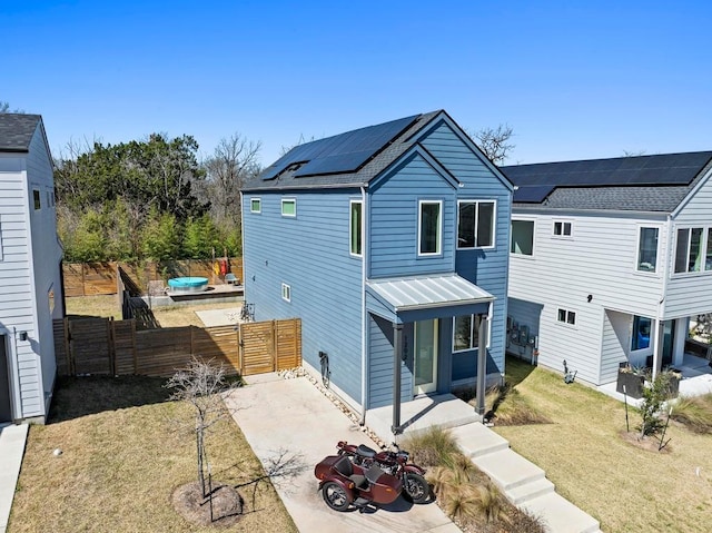 back of house featuring fence, solar panels, a standing seam roof, a yard, and metal roof