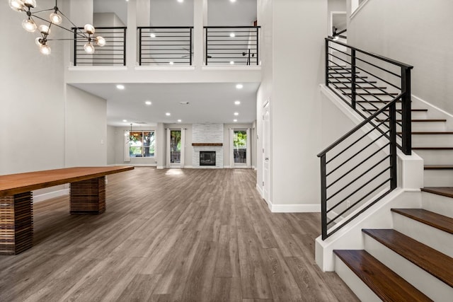 unfurnished living room with baseboards, stairs, a high ceiling, wood finished floors, and a notable chandelier