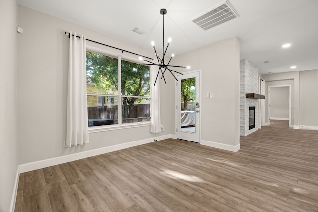 unfurnished dining area with a notable chandelier, visible vents, a wealth of natural light, and wood finished floors