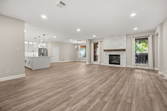 unfurnished living room with light wood-type flooring, visible vents, a wealth of natural light, and a sink