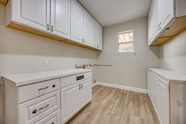 laundry room featuring washer hookup, cabinet space, light wood-type flooring, and baseboards