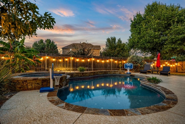 pool at dusk with a pool with connected hot tub, a fenced backyard, and a patio area