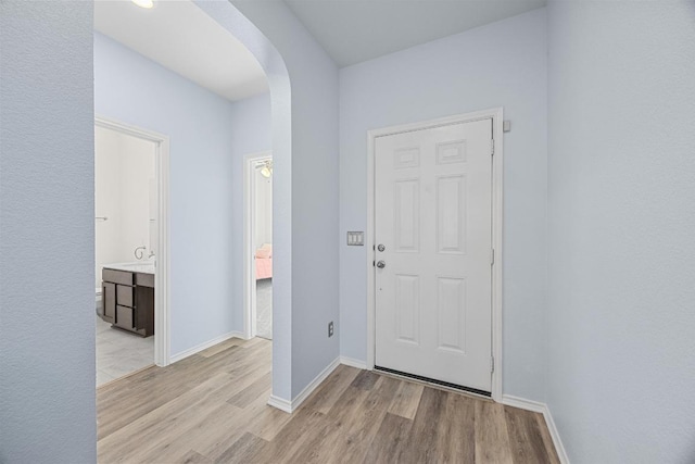 foyer featuring arched walkways, baseboards, and light wood-style floors