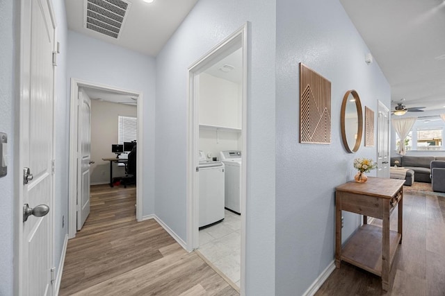 hall with washing machine and clothes dryer, visible vents, light wood-style flooring, and baseboards