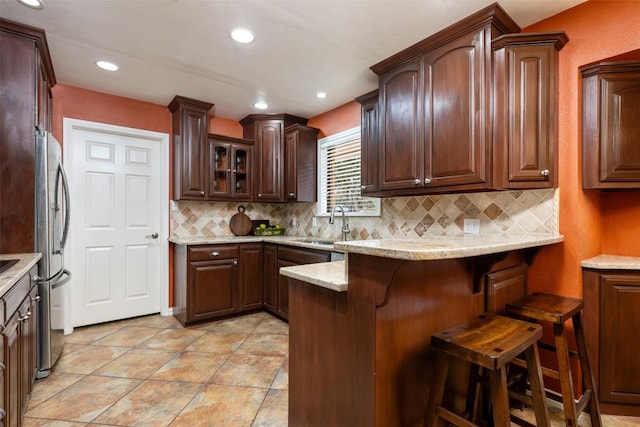 kitchen with a kitchen bar, decorative backsplash, light stone countertops, and freestanding refrigerator